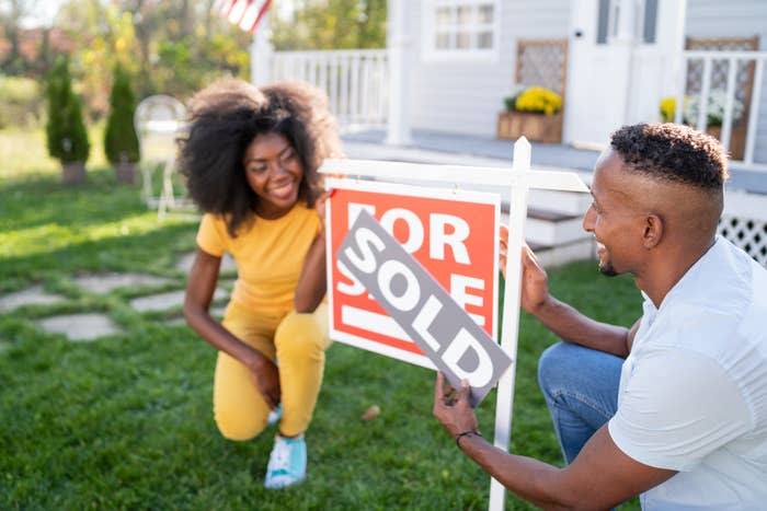 Young couple outside a house putting a "Sold" sign over the "For Sale" sign