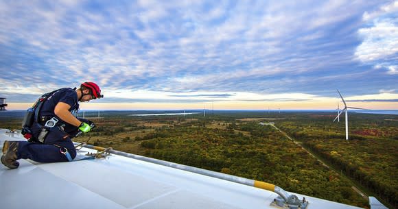 Worker on top of wind turbine with other turbines in the distance.