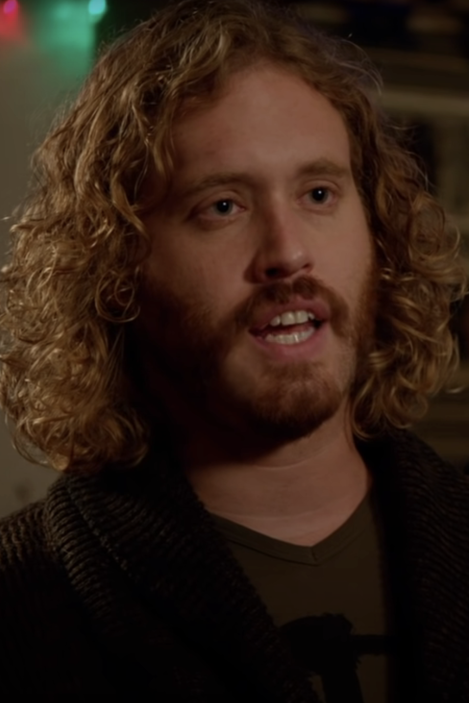 TJ in character as Erlich with curly hair in cardigan