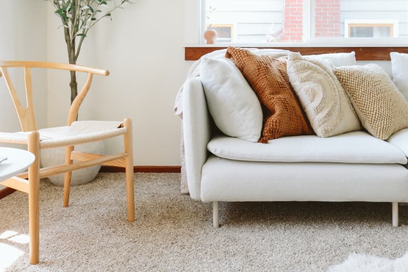 A couch inside a whit walled living room with carpeted floors.