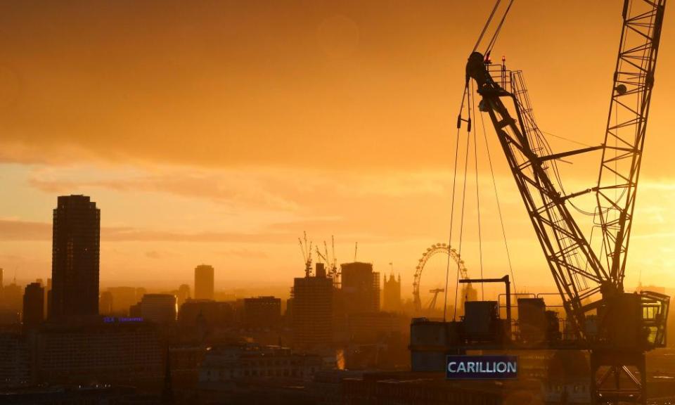 The sun sets behind a construction crane showing the branding of British construction company Carillion.