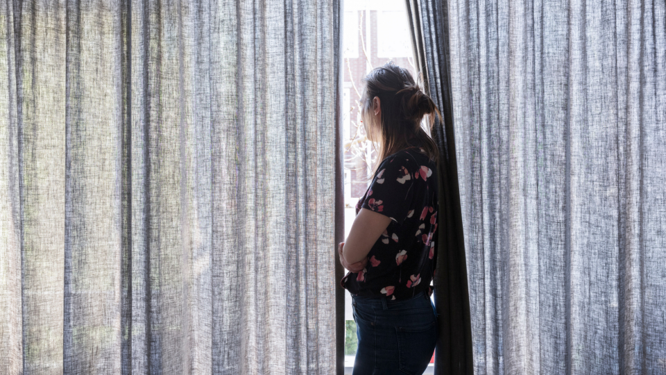 Woman looking out window with drawn curtains. Domestic violence concept.