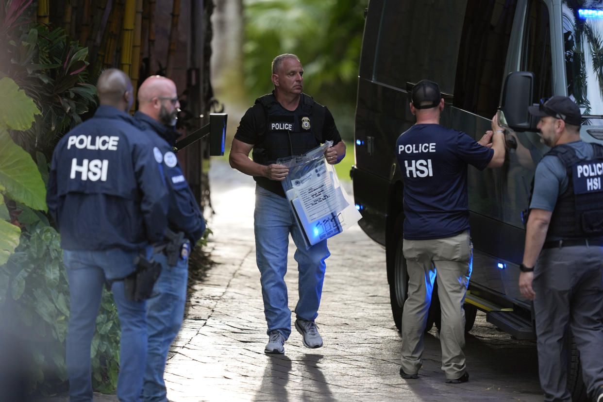 A law enforcement agent carries a bag of evidence to a van as federal agents stand at the entrance to a property belonging to Combs. 