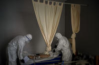 Wearing protective suits to prevent infection, mortuary workers prepare the body of an elderly person who died of COVID-19 before removing it from a nursing home in Barcelona, Spain, Friday, Nov. 13, 2020. After successfully bringing the daily death count down from over 900 in March to single digits by July, Spain has seen a steady uptick that brought deaths back to over 200 a day this month. With that relapse, the body collectors have returned to making the rounds of hospitals, homes and care facilities. (AP Photo/Emilio Morenatti)