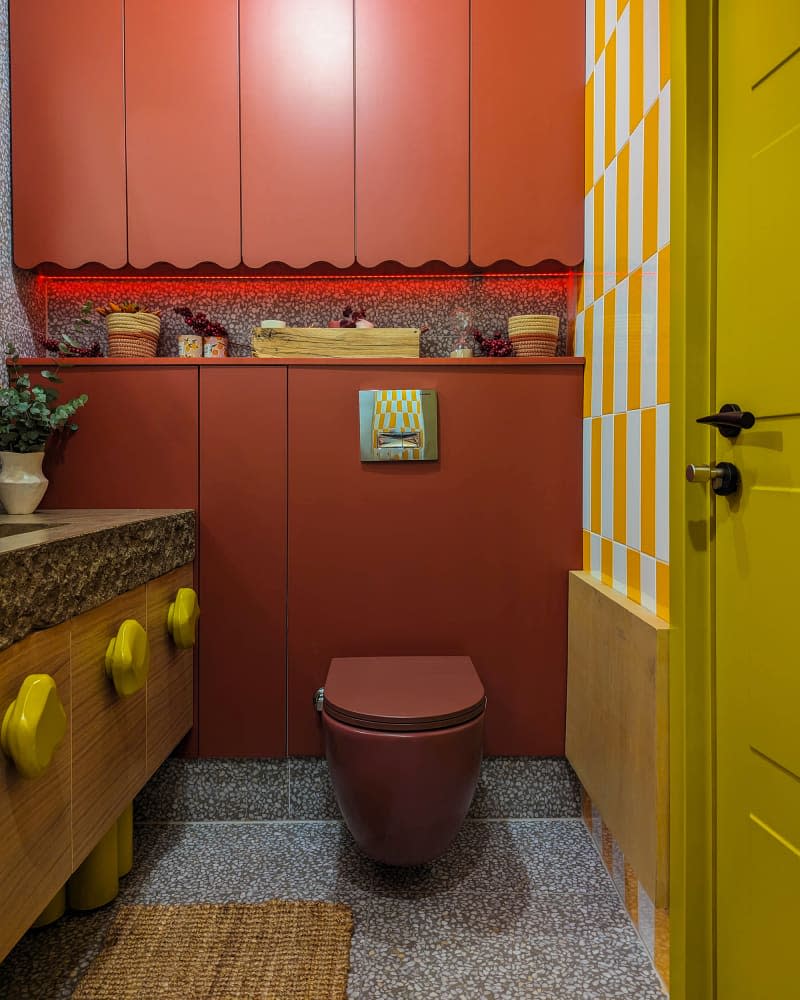 Bathroom with wavy orange and yellow mirror, wood cabinets with stone slab counter and yellow irregular shaped knobs, and lots of orange cabinets