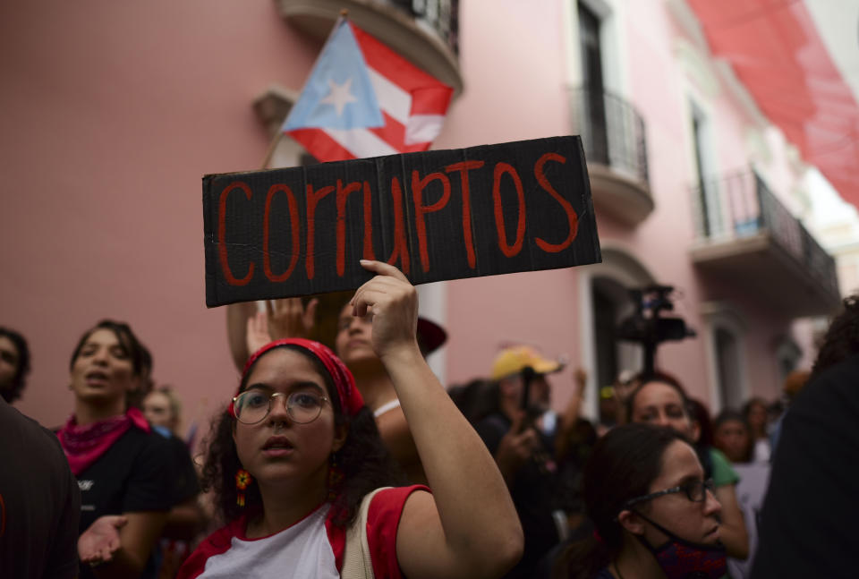 A young woman holds a sign that reads in Spanish "Corrupt" while protesting outside the executive mansion known as La Fortaleza, in Old San Juan, demanding the resignation of Governor Wanda Vazquez after the discovery of an old warehouse filled with unused emergency supplies in San Juan, Puerto Rico, Monday, Jan. 20, 2020. Anger erupted on Saturday after an online blogger posted a live video of the warehouse in the southern coastal city of Ponce filled with water bottles, cots, baby food and other basic supplies that had apparently been sitting there since Hurricane Maria battered the U.S. territory in September 2017. (AP Photo/Carlos Giusti)