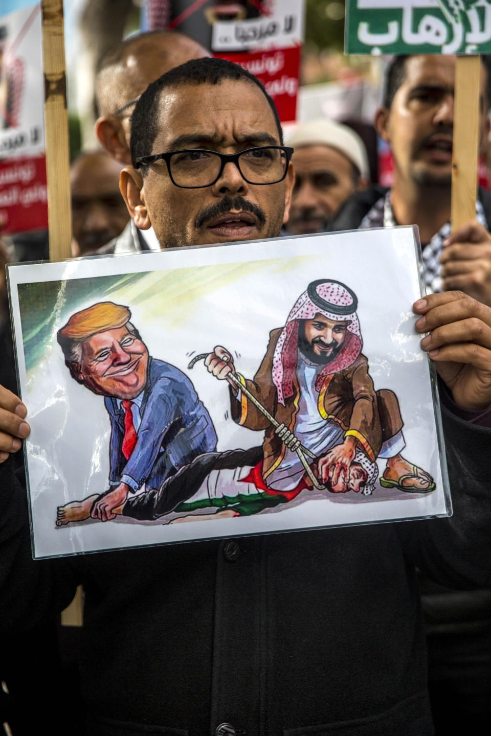 Tunisians demonstrate with poster showing Saudi Crown Prince Mohammed bin Salman and U.S President Donald Trump, Tuesday Nov. 27, 2018 in Tunis. Amid international concern about the killing of Saudi journalist Jamal Khashoggi, some 200 protesters gathered in central Tunis on Monday night to protest the prince's Tuesday arrival for talks with the Tunisian president. (AP Photo/Hassene Dridi)