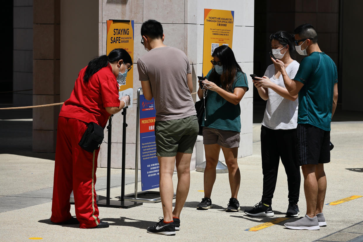 SINGAPORE - JULY 03:  Visitors wearing protective mask scan a QR code for Safe Entry check-in at the Universal Studios at Resorts World Sentosa on July 3, 2020 in Singapore. From July 1, Universal Studios Singapore reopened its door to visitors but operating capacity is limited to no more than 25 per cent as Singapore further eased the coronavirus (COVID-19) restrictions. Universal Studios is among the 13 key attractions to resume its operation in stages with safe management measures in place. As of July 3, the total number of COVID-19 cases in the country stands at 44,479.  (Photo by Suhaimi Abdullah/Getty Images)