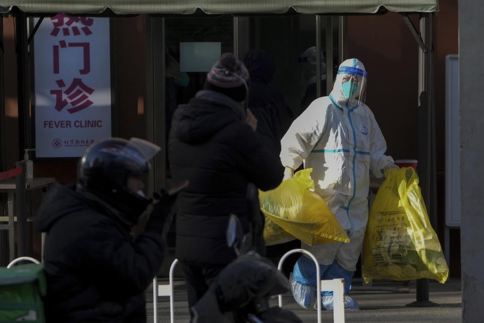 A medical worker in protective gear carries yellow bags of medical waste from a fever clinic in Beijing, Monday, Dec. 19, 2022. Chinese health authorities on Monday announced two additional COVID-19 deaths, both in the capital Beijing, that were the first reported in weeks and come during an expected surge of illnesses after the nation eased its strict "zero-COVID" approach. (AP Photo/Andy Wong)