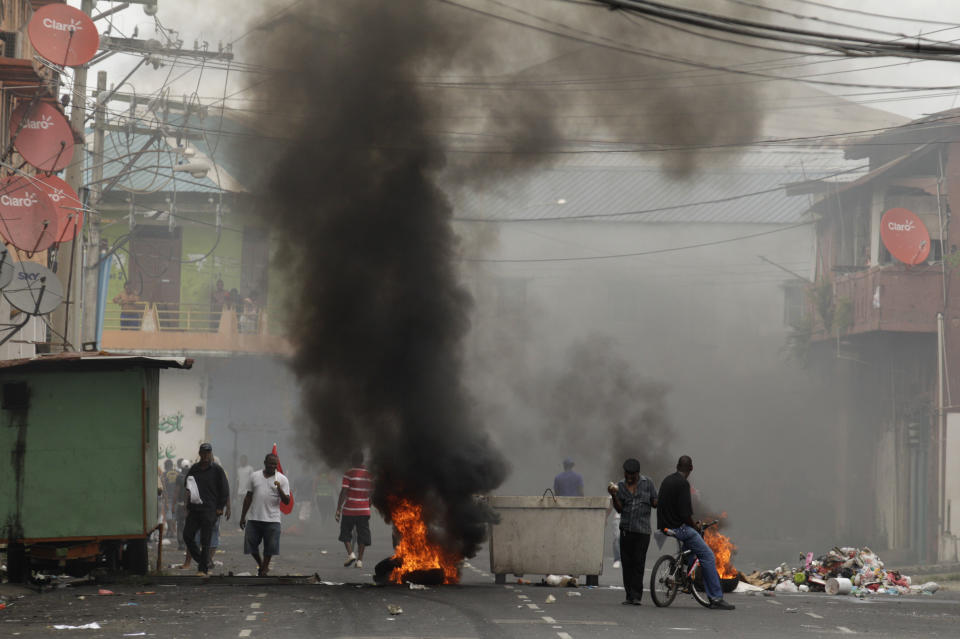 People walk past barricades set on fire by demonstrators during a protest in downtown Colon, Panama, Tuesday, Oct. 23, 2012. Demonstrators protested over a new law allowing the sale of state-owned land in the duty-free zone next to the Panama Canal. Protesters said the land is already being rented and it makes no sense to sell it. They said the government should instead raise the rent and invest the money in Colon, a poor and violent city. (AP Photo/Arnulfo Franco)