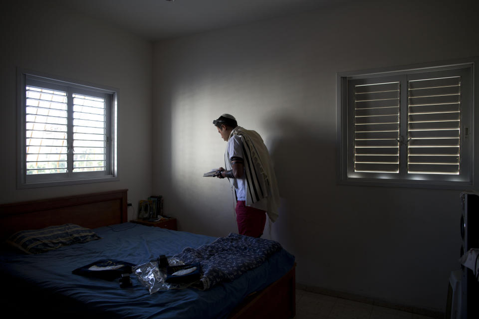 In this photo taken on Wednesday, July 31, 2013, Israeli Orthodox Jew Shahar Hadar is seem covered by a prayer shawl during a morning prayer session at his parents house in Rishon Letzion, Israel. Hadar, a telemarketer by day, has taken the gay Orthodox struggle from the synagogue to the stage, beginning to perform as one of Israel’s few religious drag queens. His drag persona is that of a rebbetzin, a female rabbinic advisor, a wholesome guise that stands out among the sarcastic and raunchy cast of characters on Israel’s drag queen circuit. (AP Photo/Oded Balilty)