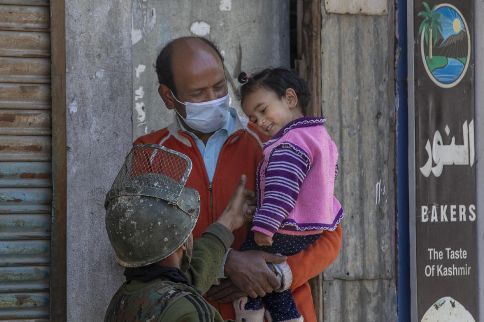 An Indian paramilitary soldier plays with a Kashmiri child during a gunbattle between Indian soldiers and suspected militants in Shopian, south of Srinagar, Indian controlled Kashmir, Friday, April 9, 2021. Seven suspected militants were killed and four soldiers wounded in two separate gunfights in Indian-controlled Kashmir, officials said Friday, triggering anti-India protests and clashes in the disputed region. (AP Photo/ Dar Yasin)