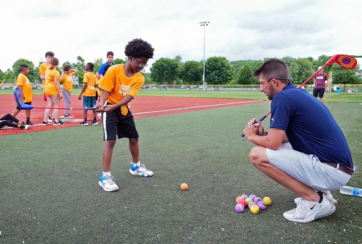 Amare Richardson learns to swing a golf club with the help of Southern Ohio PGA's Alex Heban during the Greater Columbus Sports Commission's Community Youth Camp at Berliner Sports Park. The four-day camp teaches kids to play 16 different sports.