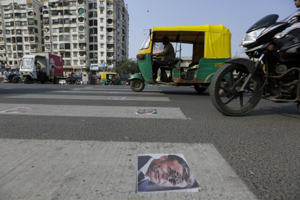 Indian commuters move on defaced images of French President Emmanuel Macron pasted by protestors on a road in Ahmedabad, India, Sunday, Nov. 1, 2020. Muslims have been calling for both protests and a boycott of French goods in response to France's stance on caricatures of Islam's most revered prophet. (AP Photo/Ajit Solanki)