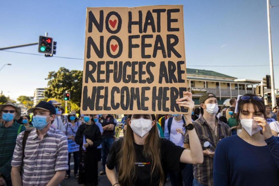 A crowd of people wearing face masks, with one holding a large sign