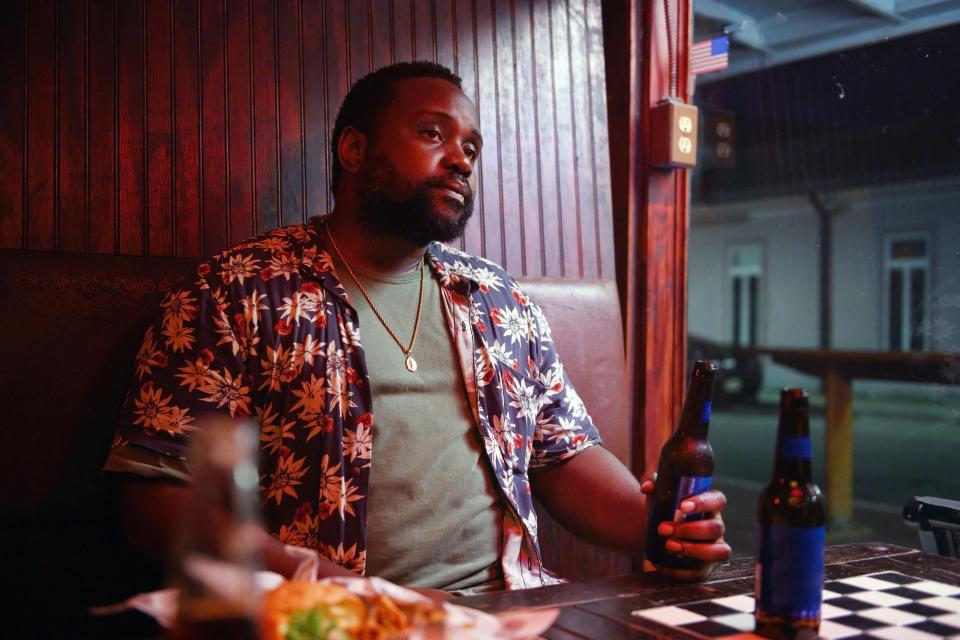 Henry sitting in a restaurant booth holding a bottle of beer in a scene in "Causeway"