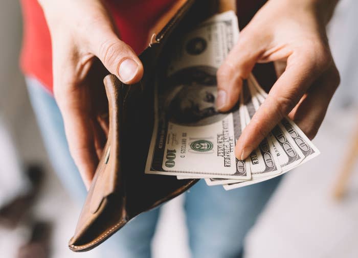 Person removing dollar bills from a brown leather wallet, symbolizing personal finance