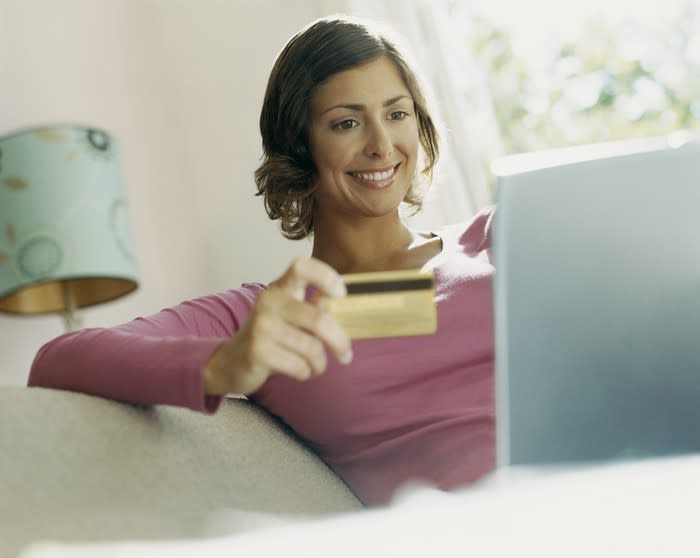 A smiling woman holding a credit card, with a laptop open on her lap