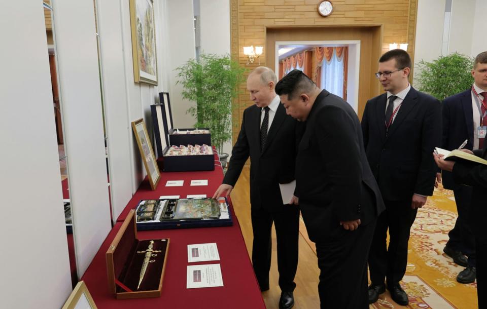 Putin presents gifts on a table to Kim Jong Un.