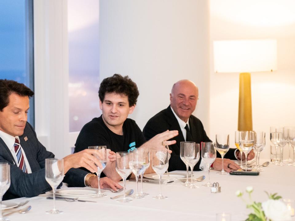 Sam Bankman-Fried is shown sitting at a long white table having dinner with Anthony Scaramucci  and Shark Tank investor Kevin O'Leary.