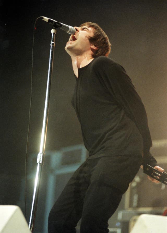 Liam Gallagher singing into a microphone, holding a tambourine 