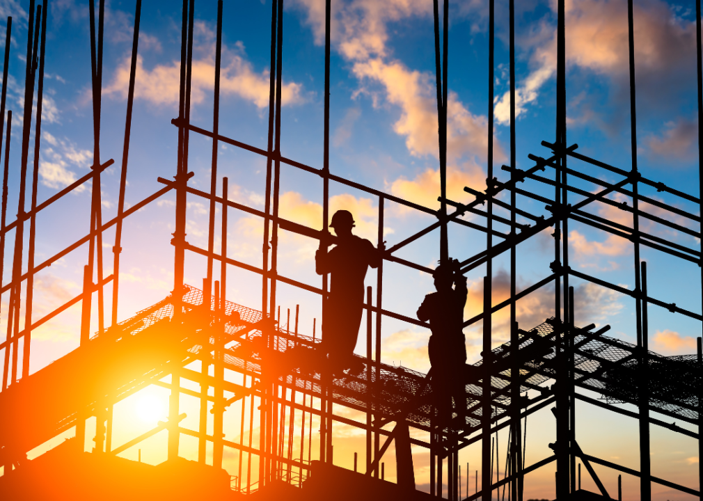 A silhouette of two construction workers on scaffolding while the sunsets behind them. 