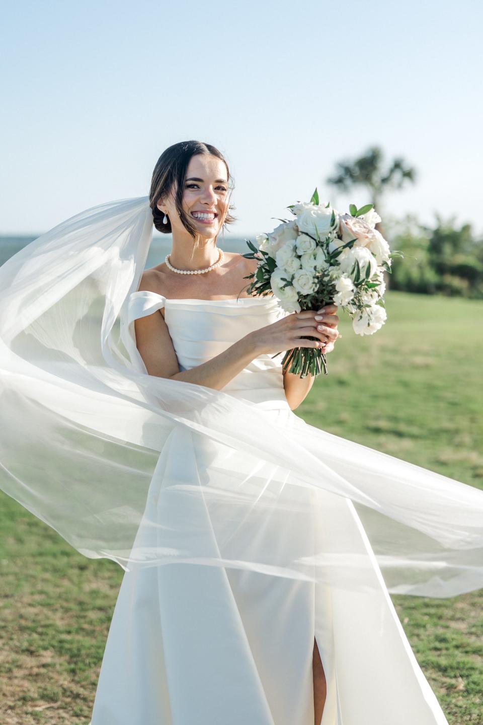 A bride smiles as her veil flies around her.