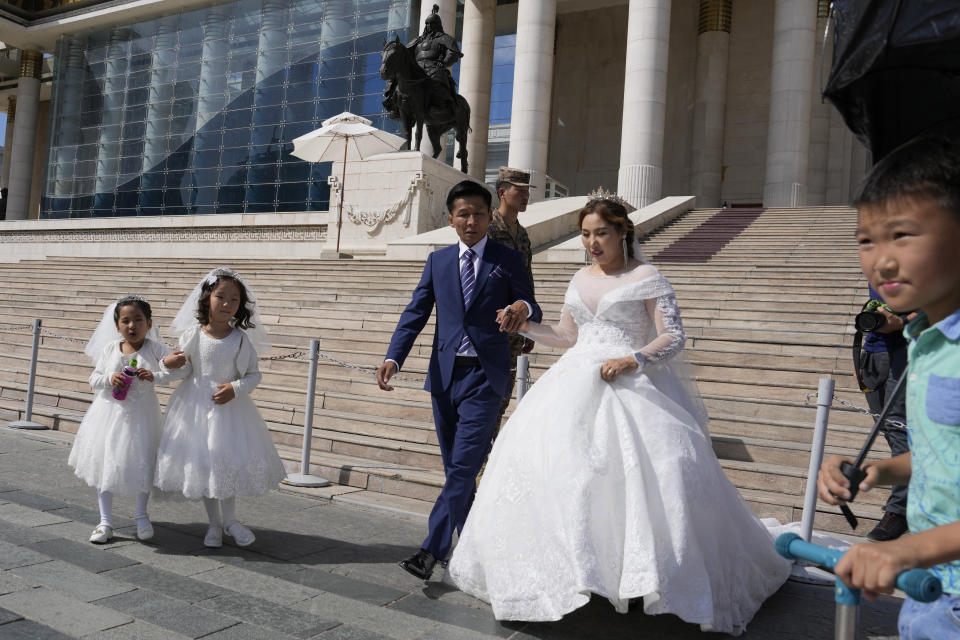 A wedding couple walks in front of the Government Palace also known as State Palace in Ulaanbaatar, Mongolia on Monday, Aug. 28, 2023. When Pope Francis travels to Mongolia this week, he will in some ways be completing a mission begun by the 13th century Pope Innocent IV, who dispatched emissaries east to ascertain the intentions of the rapidly expanding Mongol Empire and beseech its leaders to halt the bloodshed and convert.(AP Photo/Ng Han Guan)