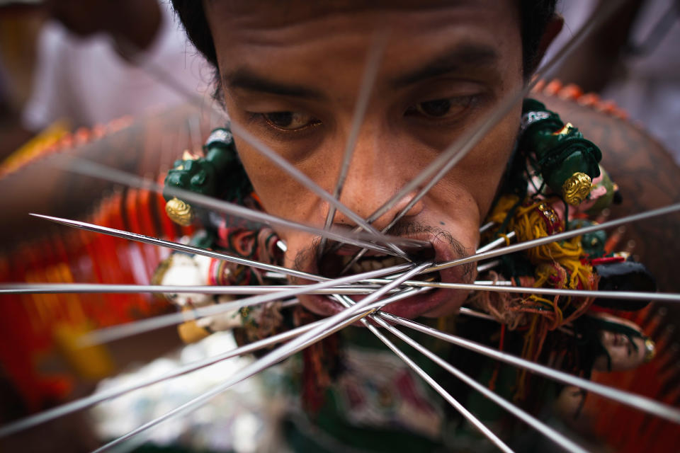 PHUKET, THAILAND - OCTOBER 05: A devotee of the Chinese shrine of Sui Boon Tong Shrine, pierces his cheeks with skewers during a procession of Vegetarian Festival on October 5, 2011 in Phuket, Thailand. Ritual Vegetarianism in Phuket Island traces it roots back to the early 1800's. The festival begins on the first evening of the ninth lunar month and lasts for nine days. Participants in the festival perform acts of body piercing as a means of shifting evil spirits from individuals onto themselves and bring the community good luck. (Photo by Athit Perawongmetha/Getty Images)