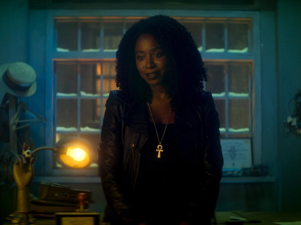 kirby howell-baptiste as death in dead boy detectives, a young woman wearing all black and a golden ankh necklace, smiling kindly