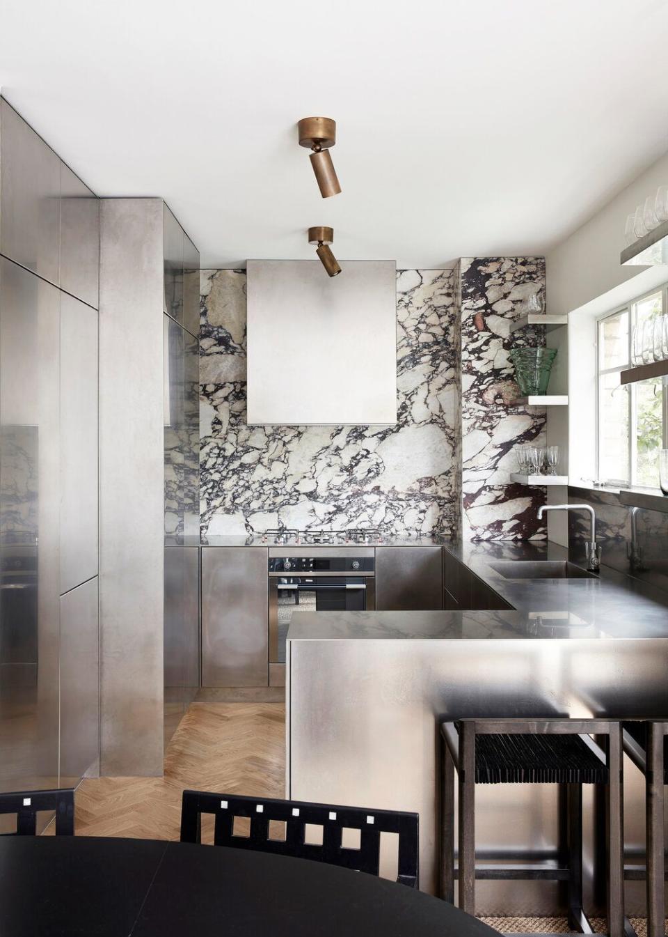 <p>Some minimalists may feel that this kitchen by Tamsin Johnson is actually more of maximalist, but it really just depends on your perspective. With an emphasis on beautiful materials, from the deep purple marble statement wall to the sleek silvery surfaces, everything is spotless, pristine, and ultra-sleek. </p>