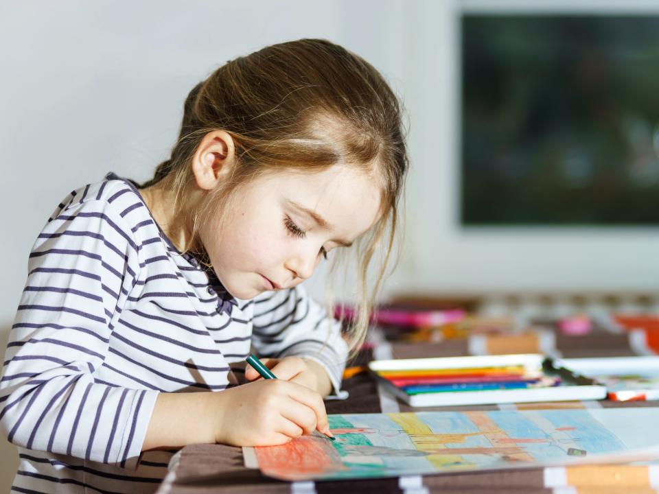 Cute little girl painting by colorful pencil at home