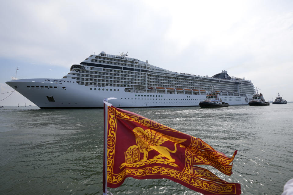 The the 92,409-ton, 16-deck MSC Orchestra cruise ship exits the lagoon as a flag of the Lion of St. Mark, the symbol of Venice, is being waved, in Venice, Italy, Saturday, June 5, 2021. The first cruise ship leaving Venice since the pandemic is set to depart Saturday amid protests by activists demanding that the enormous ships be permanently rerouted out the fragile lagoon, especially Giudecca Canal through the city's historic center, due to environmental and safety risks. (AP Photo/Antonio Calanni)