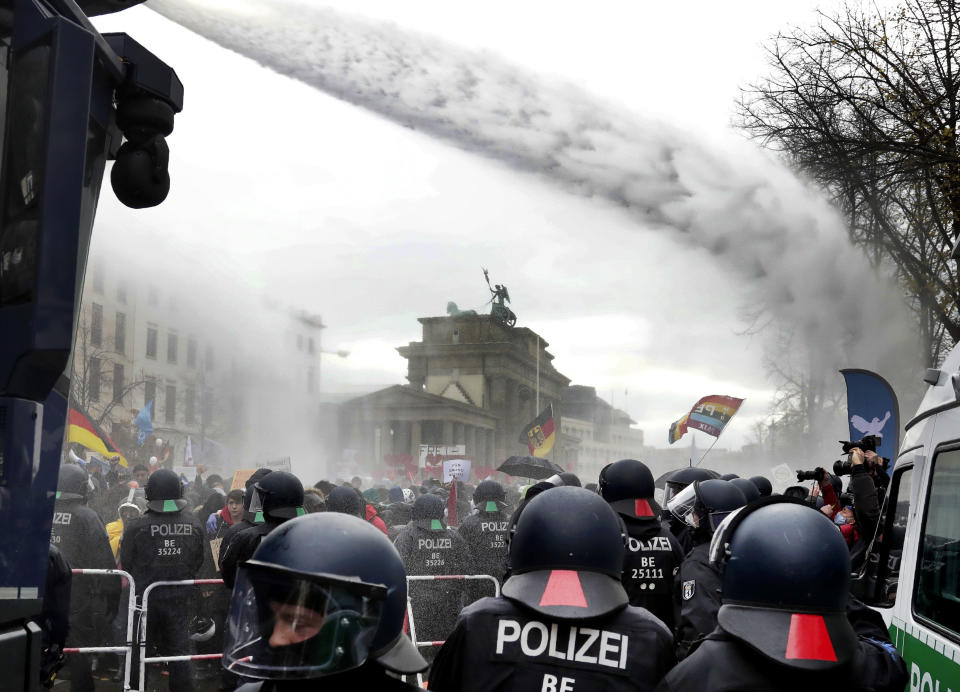 Police uses water canons to clear a blocked a road between the Brandenburg Gate and the Reichstag building, home of the German federal parliament, as people attend a protest rally in front of the Brandenburg Gate in Berlin, Germany, Wednesday, Nov. 18, 2020 against the coronavirus restrictions in Germany. Police in Berlin have requested thousands of reinforcements from other parts of Germany to cope with planned protests by people opposed to coronavirus restrictions. (AP Photo/Michael Sohn)