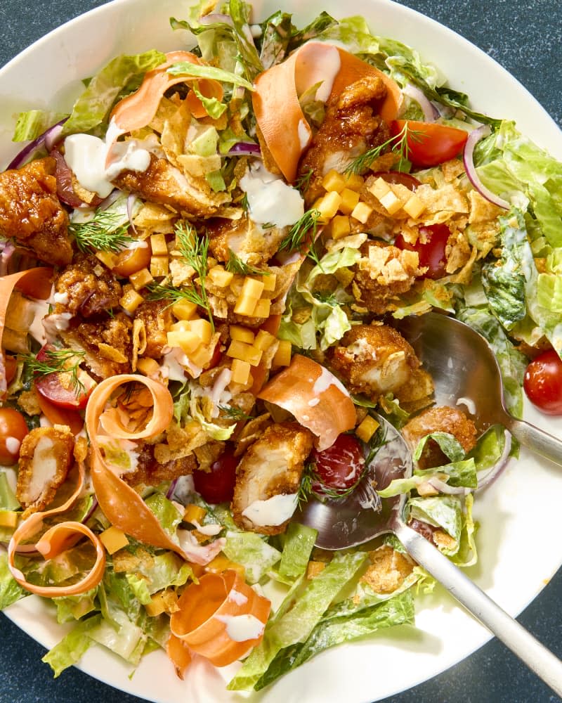 An overhead view of sticky chicken salad on a white plate on a green background with a spoon digging in.