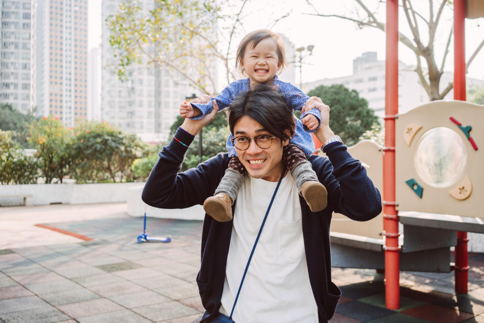 Lovely baby riding dad's shoulder joyfully in the park.