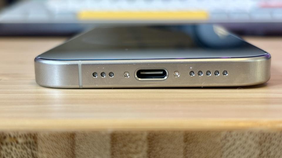 A grey titanium iPhone 15 Pro camera phone on a wooden desk