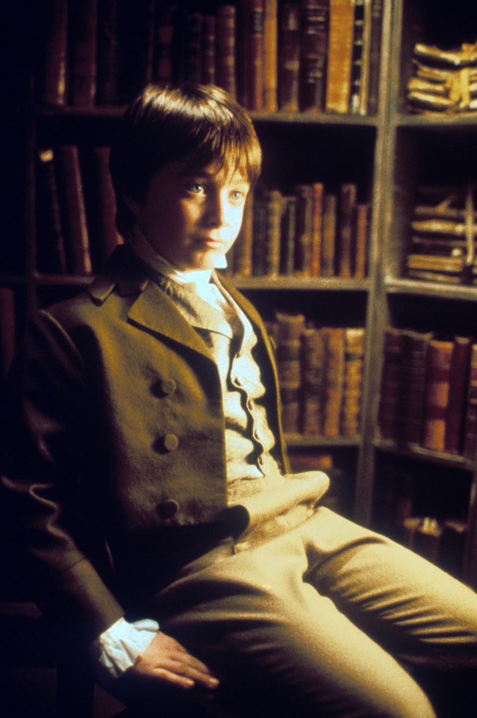 Daniel Radcliffe, in period clothing, seated in front of bookshelves