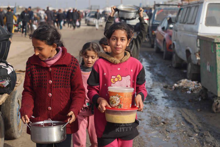 Jóvenes palestinos desplazados cargan raciones de alimentos que recibieron en un campamento improvisado en Rafah, cerca de la frontera con Egipto, en el sur de la Franja de Gaza, el 21 de enero de 2024