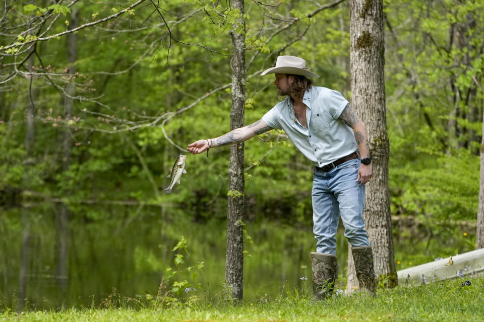 Brian Kelley tosses a fish back into a pond after catching it outside his cabin Wednesday, April 17, 2024, in Nashville, Tenn. (AP Photo/George Walker IV)