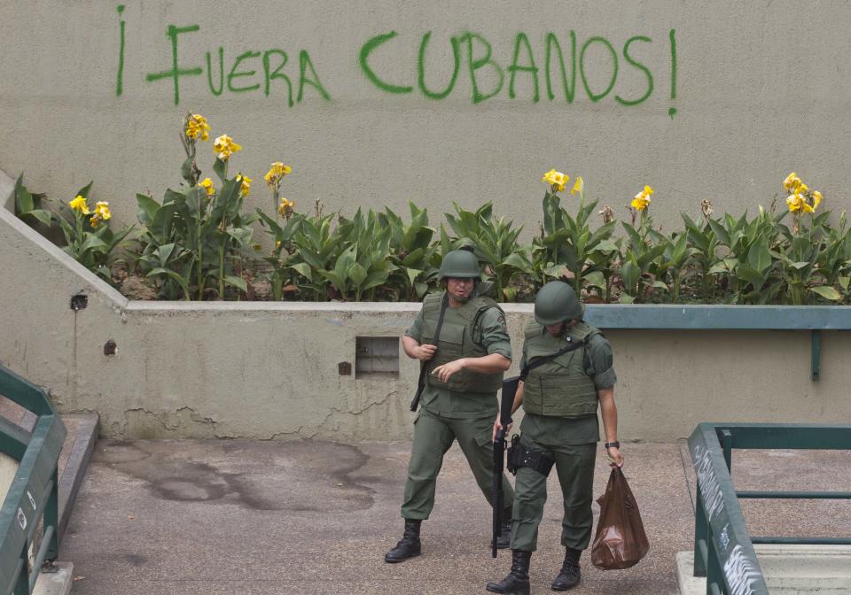 Bolivarian National Guard officers patrol Plaza Altamira after taking control of it, in Caracas, Venezuela, Monday, March 17, 2014. Government security forces took control of a Caracas plaza and surrounding neighborhoods Monday morning that had become the center of student-led protests. The graffiti on the wall reads in Spanish "Cubans Out!". Clusters of National Guardsmen were a visible presence not only on Plaza Altamira, but along the principal streets extending from it in the municipality of Chacao. (AP Photo/Esteban Felix)
