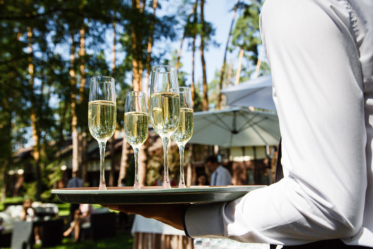 server holding champagne glasses at outdoor wedding