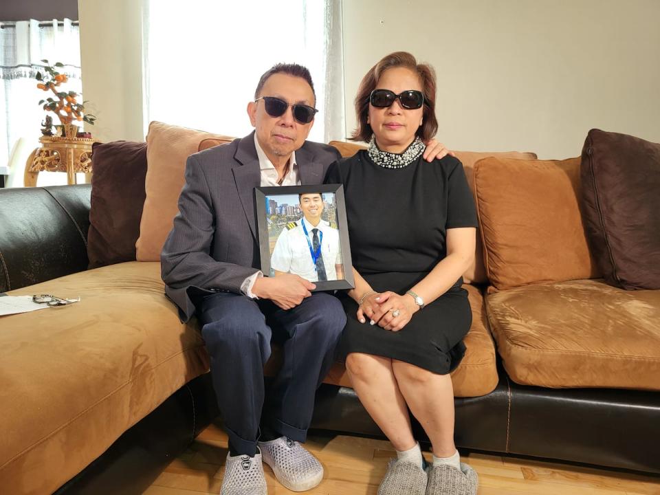 Tony and Carol Alba of Edmonton hold a photo of their son, Paszolo Alba, who was among the 6 people who died in a plane crash last week near Fort Smith, N.W.T. (Craig Ryan/CBC - image credit)