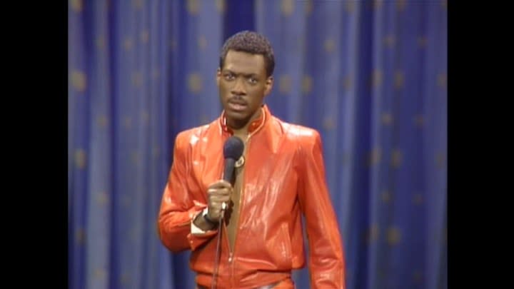 Eddie Murphy making a face in the iconic red leather suit while on stage with a mic in Eddie Murphy Delirious.