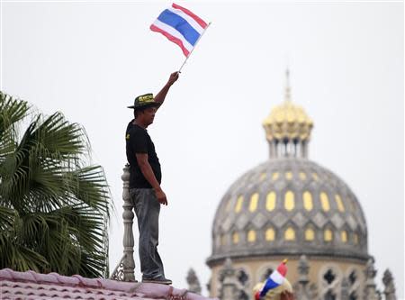 An anti-government protester waves a Thai national flag as he stands on a rooftop during a rally outside the Government House in Bangkok December 9, 2013. Thai Prime Minister Yingluck Shinawatra dissolved parliament on Monday and called a snap election, but anti-government protest leaders pressed ahead with mass demonstrations seeking to install an unelected body to run the country. REUTERS/Chaiwat Subprasom