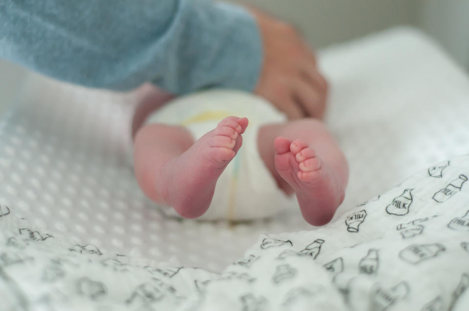 Adult's hands gently holding a baby's bare feet, with baby lying on a patterned surface