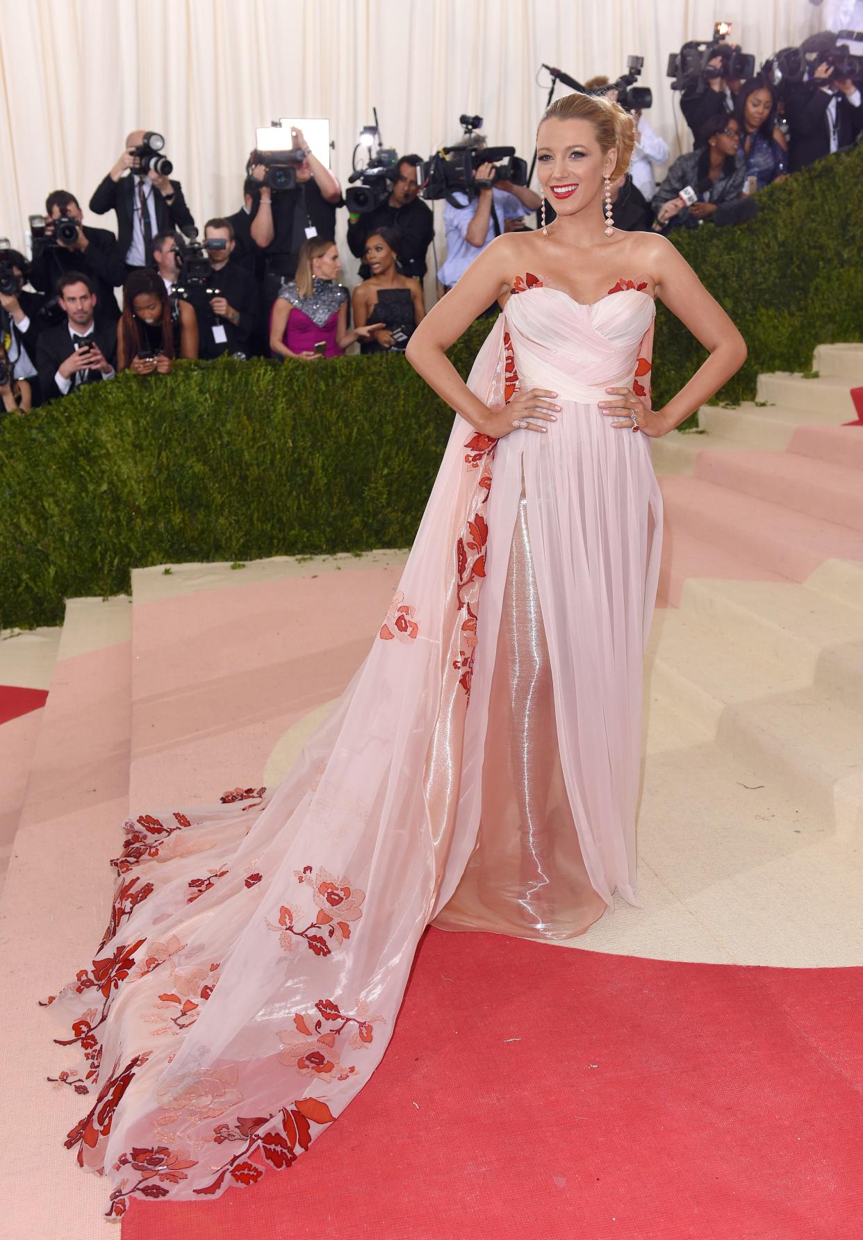 Blake Lively at the 2016 Met Gala in a pink gown with a cape with red details on it.