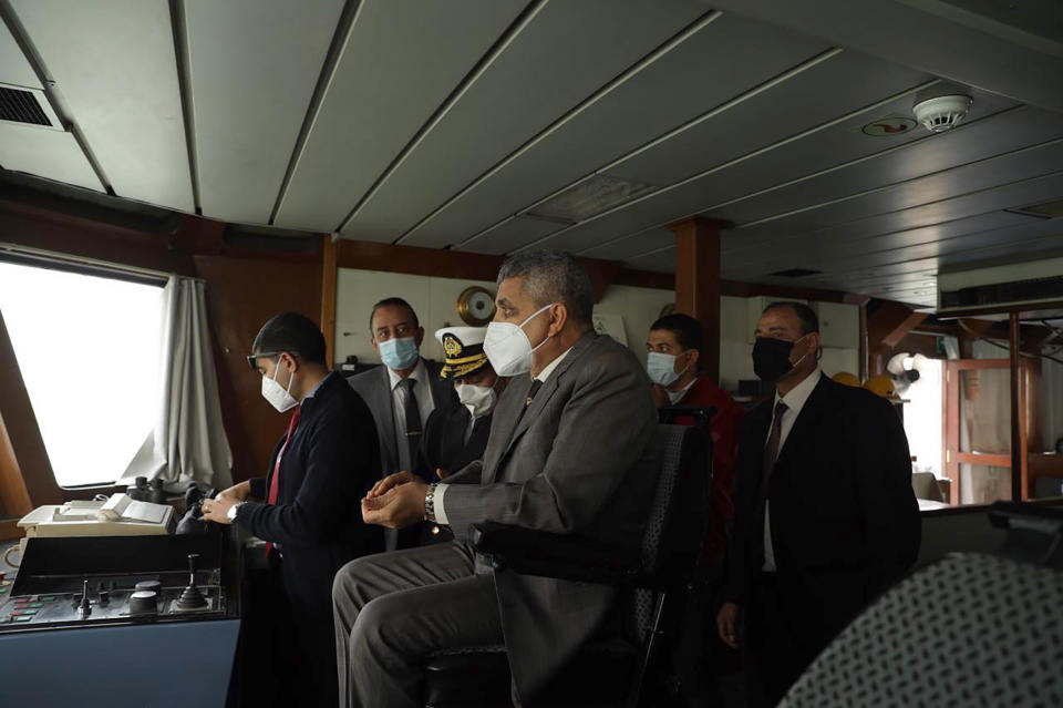 This photo released by the Suez Canal Authority on Thursday, March 25, 2021, shows the head of the Suez Canal Authority, Lt. Gen. Ossama Rabei, center, with a team look from another vessel towards the Ever Given, a Panama-flagged cargo ship, after it become wedged across the Suez Canal. An operation is underway to try to work free the ship, which further imperiled global shipping Thursday as at least 150 other vessels needing to pass through the crucial waterway idled waiting for the obstruction to clear. (Suez Canal Authority via AP)