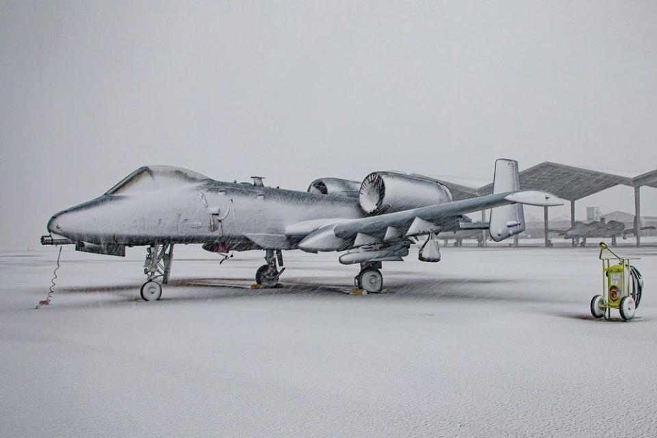 An aircraft is covered in snow parked on the flight line