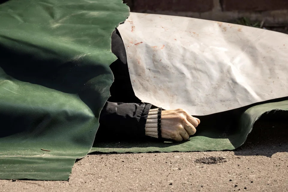 A body lies on the ground covered with plastic sheets.
